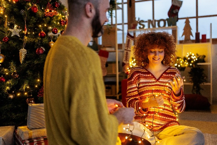 Zwei Personen entwirren eine Lichterkette vor einem Weihnachtsbaum.